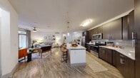 This contemporary single-floor residence is thoughtfully designed with an open-concept layout that seamlessly connects the kitchen, dining, and living areas. The kitchen is a standout feature, showcasing rich dark espresso cabinetry, stainless steel appliances, a subway tile backsplash, and a generous granite-topped island with an undermount sink and bar seating—ideal for both meal preparation and casual dining. Pendant lighting above the island adds a stylish touch, while wood-look flooring flows throughout the main living areas, enhancing the sense of continuity and warmth. The living room offers a relaxed, open atmosphere with a ceiling fan and access to natural light through nearby windows. A dedicated dining nook provides an intimate space for seated meals, accented by a bold piece of artwork. The bedroom is a comfortable retreat, featuring plush carpeting, a ceiling fan, and large windows dressed with patterned drapes that allow natural light while maintaining privacy. The full bathroom is well-appointed with a granite vanity, dark cabinetry, wood-look tile flooring, and a tiled soaking tub with a curved shower rod. A walk-in closet is conveniently accessible from the bathroom, completing this well-designed living space.