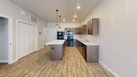 This two-story residence offers a well-organized layout spread across two floors, combining functional design with modern finishes throughout. The main floor hosts an open-concept kitchen and living area finished with light wood-style luxury vinyl plank flooring. The kitchen is a standout feature, equipped with warm-toned medium wood cabinetry, light stone-look countertops, black appliances including a refrigerator, range, microwave, and dishwasher, and a central island with pendant lighting above. Recessed ceiling lights complement the natural light admitted through multiple windows fitted with horizontal blinds, providing views of the surrounding neighborhood. A full bathroom on the main level features a wood-toned vanity with a marble-style countertop and wood-look tile flooring.

The upper floor accommodates both bedrooms, each carpeted and naturally lit by windows with blinds. The primary bedroom includes a ceiling fan with integrated lighting and dual windows. The second bedroom is a comfortable, well-proportioned space with its own window. A second full bathroom upstairs mirrors the clean, contemporary aesthetic of the first, featuring a large vanity mirror, marble-style countertop, and tile flooring. Both floors include closet storage, and a hallway connects the upper-level rooms efficiently.