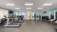 This fitness center offers a comprehensive workout environment spread across a single floor, thoughtfully designed to accommodate a wide range of exercise routines. The space is characterized by soft teal-painted walls accented with white crown molding and clean white baseboards, creating an inviting and energizing atmosphere throughout.

The main cardio area features multiple Life Fitness treadmills, elliptical machines, a stationary bike, and a rowing machine, all arranged to allow comfortable spacing between users. Large wall-mounted mirrors expand the sense of space, while several flat-screen televisions are positioned throughout for entertainment during workouts. Motivational words and definitions — including "Endurance," "Fitness," and "Determination" — are displayed as wall décor, reinforcing the facility's commitment to healthy living.

A dedicated strength training section houses a multi-station cable machine, adjustable weight benches, a power rack, and a full dumbbell rack with a variety of weights, as well as medicine balls for functional training. Natural light filters in through multiple white-shuttered windows, complemented by recessed and overhead fluorescent lighting. Glass-paned French doors connect the workout zones, promoting an open, airy flow between areas. Rubber flooring throughout provides durability and safety for all types of exercise.
