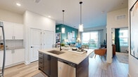 This single-floor residence offers 2 bedrooms and 3 bathrooms within a thoughtfully designed open-concept layout. Light-toned hardwood-style flooring flows throughout, creating a cohesive and airy feel across all living areas.

The kitchen serves as a central hub of the home, featuring a large island with a built-in sink, stainless steel appliances including a range, microwave, and refrigerator, crisp white shaker cabinetry, a herringbone tile backsplash, and pendant lighting. The kitchen opens directly into the living room, which is highlighted by a bold teal accent wall, large sliding glass doors that invite natural light, and direct access to an outdoor balcony.

The primary bedroom offers a comfortable footprint with natural light from multiple windows and built-in closet storage with wire shelving and hanging rods. The secondary bedroom is similarly well-appointed and naturally lit. Bathrooms feature white vanities, tile surround tub-shower combinations, and consistent black hardware accents.

Throughout the residence, recessed lighting, white raised-panel doors, and a clean, contemporary color palette contribute to a bright and cohesive overall ambiance.