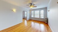 Located at 622 Harrison St in Oak Park, IL, this single-floor space showcases classic architectural character throughout. Gleaming hardwood floors run continuously across the living areas, complemented by crisp white walls, substantial crown molding, and traditional baseboard trim that speak to the building's timeless design. The spacious living room draws immediate attention with its elegant arched doorway, ceiling fan, wall sconces, and a generous bank of windows fitted with blinds that allow abundant natural light while maintaining privacy. A cast-iron radiator adds to the period charm. The adjoining dining area features a chandelier and its own radiator, creating an inviting atmosphere. The bedrooms continue the hardwood flooring and offer ceiling fans, wall sconces, and bright windows with views of the surrounding greenery. The kitchen is well-equipped with white cabinetry, grey stone countertops, tile backsplash, stainless steel appliances, and a back door that lets in additional natural light. The bathroom is cleanly finished in white tile, featuring a tub-shower combination and a radiator, with a frosted window for privacy. Throughout, the space maintains a cohesive, classic aesthetic rooted in early 20th-century Oak Park architecture.