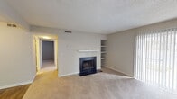 Located at 227 Wind Rd in Greensboro, NC, this single-floor home offers a practical and comfortable layout throughout. The living room serves as the heart of the space, featuring a classic wood-burning fireplace with a clean white mantel and a dark surround, flanked by built-in shelving perfect for display or storage. Soft wall-to-wall carpeting adds warmth underfoot, while a large sliding glass door fitted with vertical blinds allows natural light to fill the room and provides access to the outdoors. A textured ceiling is consistent throughout the main living areas. The kitchen is efficiently designed with ample white cabinetry reaching to the ceiling, light countertops, a stainless steel sink, and white appliances including a refrigerator and electric range with a range hood above. Wood-look flooring in the kitchen extends into the bathroom, which features a tub-shower combination with white tile surround, safety grab bars, a wall-mounted vanity sink, and a large mirror with overhead lighting. The bedrooms are carpeted and bathed in natural light through multiple windows with blinds, offering a calm and neutral setting. The overall aesthetic is clean and understated, with a neutral color palette of warm grays and beiges carried consistently throughout the home.