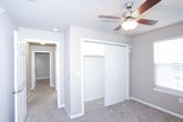 This single-floor residence offers a practical and comfortable layout with well-defined living spaces. The kitchen is equipped with a black Frigidaire electric coil range, a built-in overhead vent hood, warm wood-toned cabinetry, and light-colored countertops — providing a functional cooking environment with ample storage. The living area features plush wall-to-wall carpeting, neutral beige walls, a textured ceiling, and a large window fitted with horizontal blinds that allows generous natural light to fill the room. A ceiling fan is present in the connected area, enhancing airflow and comfort. The bedroom is similarly carpeted and bathed in natural light through a sizable window, offering a clean, open feel with smooth neutral walls and white trim throughout. A closet provides convenient storage directly off the bedroom. The bathroom is neatly appointed with wood-look vinyl flooring, a full tub-shower combination with white tile surround, a toilet, and a vanity with dark cabinetry. The dollhouse view reveals a cohesive, efficiently designed floor plan that connects all areas logically, making the space easy to navigate. Clean finishes and consistent neutral tones throughout create a calm, move-in-ready atmosphere.