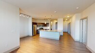 This single-floor residence offers a thoughtfully designed open-concept layout that seamlessly connects the living, dining, and kitchen areas. The kitchen is a standout feature, equipped with a full suite of stainless steel appliances — including a refrigerator, range, and over-the-range microwave — complemented by rich dark-toned cabinetry, granite countertops, and a tile backsplash. A large central island with a built-in sink and additional counter space serves as the heart of the kitchen, ideal for both meal preparation and casual dining. Track and pendant lighting illuminate the space with a modern touch. Hardwood-style flooring flows throughout the main living areas, adding warmth and continuity, while plush carpeting provides comfort in the bedrooms. The bedrooms are generously sized, each featuring closet storage and access to the well-lit hallway corridor. The bathroom includes a full soaking tub and shower combo with clean white tile surround and brushed nickel fixtures. A dedicated utility area in the hallway provides in-unit laundry convenience. Large windows throughout allow for ample natural light, contributing to the bright and airy atmosphere of this well-appointed residence.