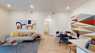This thoughtfully designed single-floor unit offers a bright and contemporary living experience with a cohesive aesthetic carried throughout. The open-concept living and dining area serves as the heart of the space, featuring light hardwood flooring, recessed lighting, and crisp white walls that create an airy, welcoming atmosphere. Large sliding glass doors in the living area flood the space with natural light and provide access to an outdoor area. The dining space comfortably accommodates a round wooden table paired with navy upholstered chairs, flowing seamlessly into the living room.

The kitchen is outfitted with gray shaker-style cabinetry, white quartz countertops, a classic white tile backsplash, and stainless steel appliances, offering both style and functionality. Two bedrooms provide comfortable retreats; the primary bedroom features plush carpeting, generous ceiling height, and a walk-in closet, while the second bedroom benefits from a large window with ample natural light. Two bathrooms serve the unit — one featuring a vanity with sage-green cabinetry and a framed mirror, and the other a full tub-shower combination with warm wood-tone flooring. A smart thermostat and modern fixtures complete this well-finished space.