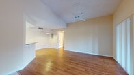 This single-floor residence offers a well-organized layout designed for comfortable everyday living. The open-concept living and dining area is a standout feature, showcasing warm hardwood flooring, soaring vaulted ceilings, and a ceiling fan that enhances airflow throughout the space. Large sliding glass doors flood the living area with natural light and provide access to an outdoor patio, while a nearby closet with louvered doors adds convenient storage. The transition between tile and hardwood flooring marks the entry zone, which connects seamlessly to the rest of the unit. The kitchen is efficiently designed with white cabinetry, a full suite of white appliances including a range, microwave, and refrigerator, and granite-style countertops. A breakfast bar peninsula opens the kitchen toward the living area, promoting a connected, social atmosphere. The bedrooms feature neutral-toned carpet, ceiling fans, and windows with vertical blinds that allow for natural light and privacy. The bathroom is clean and functional, complete with a tiled tub and shower combination, a toilet, and a vanity with granite-style countertops. Throughout the unit, warm beige walls and consistent finishes create a cohesive and inviting ambiance.