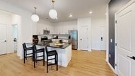 Located at 720 River Hwy in Mooresville, NC, this thoughtfully designed 2-bedroom, 3-bathroom residence offers a cohesive blend of modern style and everyday functionality across a single floor. The open-concept layout connects the kitchen and living area seamlessly, with light hardwood-style flooring flowing throughout. The kitchen is outfitted with crisp white cabinetry, dark granite countertops, stainless steel appliances including a full-size refrigerator and range, a subway tile backsplash, and a central island illuminated by globe pendant lights. The living area is anchored by bold teal accent walls and a ceiling fan, creating a vibrant yet comfortable atmosphere with ample natural light from large windows. The primary bedroom features plush carpeting, a teal-painted ceiling, natural light from double windows, and access to a well-appointed en-suite bathroom with dark granite countertops and white cabinetry. The second bedroom continues the bold aesthetic with deep navy walls, a ceiling fan, and generous closet space. Closets feature wire shelving systems for organized storage. A dedicated laundry room houses a full-size washer and dryer. The bathrooms are finished with matte black fixtures, including a soaking tub with tiled surround. This residence offers a refined, design-forward living experience in a convenient Mooresville location.
