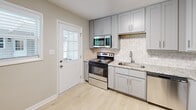 Located at 705 Buck Jones Rd in Raleigh, NC, this 2-bedroom, 1-bathroom home offers a well-organized single-floor layout. Light hardwood flooring runs throughout, complementing the neutral wall tones and clean white trim that give the space a bright, cohesive feel. The living room is a standout area, highlighted by a dramatic full-length exposed brick accent wall and crown molding, adding texture and character to the otherwise modern interior. Natural light filters in through multiple windows, enhancing the open atmosphere. The kitchen is thoughtfully appointed with gray shaker-style cabinetry, granite countertops, a classic subway tile backsplash, and stainless steel appliances including a range, microwave, and dishwasher. A glass-panel exterior door in the kitchen provides additional natural light and outdoor access. Both bedrooms are comfortably sized, each featuring closets with built-in rods and shelving, and windows that bring in views of the surrounding greenery. Mini-split HVAC units ensure efficient climate control throughout. The bathroom includes a full tub-shower combination with white tile surround and a window for ventilation. A connecting hallway ties the layout together for a practical and functional flow.