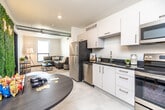 This contemporary single-floor unit offers a well-designed layout that blends functionality with modern style. The open-concept kitchen flows seamlessly into the living area, creating a cohesive and inviting communal space. The kitchen is outfitted with sleek white cabinetry, dark granite countertops, stainless steel appliances including a refrigerator, electric range, dishwasher, and microwave, along with a double undermount sink. Exposed ductwork on the ceiling adds an industrial design touch that complements the unit's modern character. Light tile flooring runs throughout the main living areas, enhancing the bright, airy atmosphere. The living room features a large window with city views, filling the space with natural light. Multiple bedrooms offer comfortable accommodations, each with light carpet, natural light from windows with blinds, and access to city views. Bedrooms are well-proportioned and versatile, accommodating both sleeping and workspace arrangements. Two bathrooms mirror each other in design, featuring white vanity cabinetry, dark granite countertops, undermount sinks, large mirrors, and clean tile flooring — delivering a polished, uniform finish throughout. The overall ambiance is modern, clean, and practical.