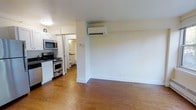 This single-floor, 1-bedroom, 1-bathroom unit offers a practical and well-organized layout. The open living area features warm hardwood flooring that extends throughout, creating a cohesive and inviting atmosphere. A wall-mounted mini-split air conditioning unit provides efficient climate control directly in the main living space.

The kitchen is positioned adjacent to the living area and is equipped with stainless steel appliances, including a gas range with oven and an over-the-range microwave. White cabinetry lines the upper and lower portions of the kitchen, offering ample storage space. The kitchen flows naturally into the rest of the unit, making it accessible and functional for everyday use.

A glimpse into the bathroom reveals a tiled space with basic fixtures, maintaining a clean and utilitarian design. The corridor connecting the rooms is compact and efficient, making good use of the available floor plan.

The unit's neutral white walls and light-toned ceiling contribute to a bright and airy feel, while the hardwood floors add a touch of warmth. Overall, the space is thoughtfully arranged to maximize functionality within a cozy footprint, making it well-suited for single occupants or couples seeking a straightforward and comfortable living environment.