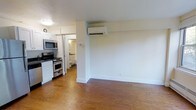 This single-floor, 1-bedroom, 1-bathroom unit offers a practical and well-organized layout. The open living area features warm hardwood flooring that extends throughout, creating a cohesive and inviting atmosphere. A wall-mounted mini-split air conditioning unit provides efficient climate control directly in the main living space.

The kitchen is positioned adjacent to the living area and is equipped with stainless steel appliances, including a gas range with oven and an over-the-range microwave. White cabinetry lines the upper and lower portions of the kitchen, offering ample storage space. The kitchen flows naturally into the rest of the unit, making it accessible and functional for everyday use.

A glimpse into the bathroom reveals a tiled space with basic fixtures, maintaining a clean and utilitarian design. The corridor connecting the rooms is compact and efficient, making good use of the available floor plan.

The unit's neutral white walls and light-toned ceiling contribute to a bright and airy feel, while the hardwood floors add a touch of warmth. Overall, the space is thoughtfully arranged to maximize functionality within a cozy footprint, making it well-suited for single occupants or couples seeking a straightforward and comfortable living environment.