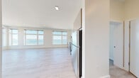 This thoughtfully designed single-floor residence offers a clean, contemporary aesthetic throughout its well-organized layout. The open-concept living and kitchen area serves as the heart of the home, featuring light-toned hardwood flooring, recessed lighting, and a wall of large picture windows that frame breathtaking waterfront views of the open ocean. The kitchen is equipped with stainless steel appliances, including a full-size refrigerator and range, complemented by light wood cabinetry that extends to the ceiling for ample storage.

The bedroom is carpeted for comfort and opens directly onto a private balcony through floor-to-ceiling sliding glass doors, offering unobstructed panoramic views of the beach and water beyond. A second bedroom features light hardwood flooring and a generously sized window overlooking a vibrant cityscape.

Two bathrooms serve the residence: one features a glass-enclosed walk-in shower with vertically laid white subway tile and warm stone-tiled flooring, while the second includes a full soaking tub finished with matching white tile surround and chrome fixtures. Throughout the space, a neutral white and warm beige palette, abundant natural light, and modern finishes create a serene, move-in-ready atmosphere.