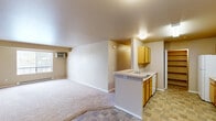 Located at 1636 S Main St in Moscow, Idaho, this two-bedroom, one-bathroom unit offers a functional and well-organized layout across a single floor. The open-concept living and kitchen area forms the heart of the unit, where neutral-toned carpet flows through the spacious living room, which features a window with natural light and a wall-mounted AC unit. The kitchen is efficiently designed with warm wood-toned cabinetry, white appliances including a refrigerator, electric range, microwave, and dishwasher, plus a peninsula with a built-in sink that separates the cooking space from the living area. Tile flooring runs through the kitchen, adding durability to the high-traffic zone. A dedicated pantry closet provides generous dry storage. The two bedrooms are carpeted and finished with neutral walls, offering a calm, understated ambiance. Each room is served by its own closet, including a walk-in closet with wrap-around shelving and hanging rods. The bathroom features a wide vanity with oak cabinetry, a large mirror, and a shower-tub combination, all finished with tile flooring. Baseboard heating is present throughout, ensuring comfort year-round in the Idaho climate.