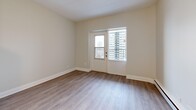 This efficiently laid-out one-bedroom, one-bathroom unit offers a clean, modern aesthetic across a single floor. Light-toned hardwood flooring runs throughout, complementing the neutral palette of warm white and beige walls that create a bright, cohesive feel.

The living room is a comfortable, open area featuring a glass door that opens onto a private balcony with urban views, as well as an additional window that brings in natural light. Baseboard heating is present throughout the unit.

The kitchen is thoughtfully designed with white shaker-style cabinetry, stainless steel appliances including a full-size refrigerator, built-in microwave, and a stove with oven. A stacked washer and dryer unit is conveniently integrated within a dedicated closet space directly adjacent to the kitchen, providing in-unit laundry.

The hallway connects the main living areas to the private spaces and features built-in closet storage on both sides, maximizing organizational capacity. The bedroom is a well-proportioned room with a large sliding-door closet and a window for natural light.

The bathroom is finished with clean white subway tile surrounding a full soaker tub and shower combination with chrome fixtures, maintaining the unit's crisp, contemporary style throughout.