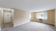 Located at 6121 Eastman Ave in Midland, Michigan, this two-bedroom, one-bathroom unit offers a functional and straightforward single-floor layout. The living room is generously proportioned, featuring wall-to-wall carpet, neutral beige walls, and a large window fitted with vertical blinds that allow natural light to filter in alongside outdoor greenery views. A baseboard heating system and wall-mounted AC unit ensure year-round comfort. The living area flows into a combined dining and kitchen space, where warm wood-toned cabinetry and a white refrigerator provide practical storage and workspace. Both bedrooms are carpeted and share the same warm neutral palette, each equipped with windows overlooking outdoor greenery and baseboard heating. The primary bedroom offers a notably comfortable footprint, complete with a dedicated closet. Altogether, the unit features four closets, providing ample storage throughout. The full bathroom is finished with white subway-style wall tile surrounding a tub/shower combination, paired with clean white fixtures. A hallway connects the main areas, contributing to the unit's efficient flow. The overall ambiance is clean, bright, and move-in ready, well-suited for comfortable everyday living.