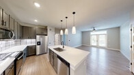 Located in Austin's vibrant 78702 zip code, this modern 2-bedroom, 2-bathroom single-story home offers a thoughtfully designed open-concept layout. The combined kitchen and living area serves as the heart of the home, featuring a large center island with a white quartz countertop, undermount sink, and sleek pendant lighting. The kitchen is well-appointed with gray shaker-style cabinetry, a subway tile backsplash, and a full suite of stainless steel appliances, including a refrigerator, electric range, microwave, and dishwasher. Light wood-look flooring flows throughout, complementing the neutral color palette and lending a clean, contemporary feel. The living area is bright and airy, illuminated by natural light from a set of glass patio doors and a ceiling fan overhead. Both bedrooms are comfortably sized, each with natural light from windows with blinds and ceiling fans. The primary bedroom connects conveniently to a walk-in closet outfitted with built-in shelving and hanging rods. The two bathrooms feature tile flooring, white vanities, and matte black hardware accents, with one offering a tub-shower combination with vertically laid white tile surround.