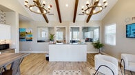 The Parke Place leasing office is a single-story space thoughtfully designed to create a warm and professional first impression for prospective residents. The interior is anchored by vaulted ceilings adorned with dark wood exposed beams, lending architectural character throughout. Two matching circular bronze-and-glass chandeliers illuminate the main reception area, casting a refined glow over light wood-look flooring that runs throughout the space.

The reception desk is a standout feature — a crisp white shaker-panel station with a dark countertop, flanked by pass-through windows that offer a view into the working office behind. The staff area is equipped with cabinetry and workstations, maintaining an organized and functional backdrop.

A comfortable lounge area provides seating with plush boucle accent chairs arranged around a round coffee table on a patterned area rug, beneath a wall-mounted display screen showcasing community imagery and branding. Natural light filters in through multiple white-shuttered windows throughout.

A separate hospitality area features a rustic wood communal table with industrial-style metal chairs, white cabinetry, and a striking patterned tile accent wall that adds a bold decorative focal point. The entrance door is glass-paneled, displaying office hours and the Parke Place logo, further reinforcing the community's branded identity.