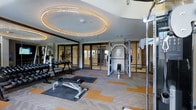 This contemporary fitness center is thoughtfully designed to deliver both functionality and aesthetic appeal. The space is anchored by a striking oval recessed ceiling feature adorned with warm LED strip lighting, creating an eye-catching focal point that lends the room a refined, upscale atmosphere. The ceiling's curved contours add an architectural elegance rarely found in gym environments.

The flooring consists of a patterned carpet tile layout in a mix of grey and bold orange tones, providing both comfort underfoot and a dynamic visual energy throughout the space. Floor-to-ceiling mirror panels line one wall, enhancing the sense of openness and allowing users to monitor their form during exercise.

The equipment offering is comprehensive, including a dumbbell rack with a full range of free weights, an adjustable workout bench, and a multi-function cable and weight machine, catering to a wide variety of strength training needs. Large glass-panel doors and walls connect the fitness area to adjacent spaces, maintaining an open, airy feel while allowing ample natural light to filter through.

The overall ambiance is clean, modern, and well-maintained, reflecting a high standard of design and upkeep. This fitness center is well-suited for residents or guests seeking a professional-grade workout environment.