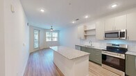Located at 211 Hammond Center Dr in Raleigh, NC, this well-appointed one-bedroom, one-bathroom residence offers a thoughtfully designed open-concept layout with modern finishes throughout. Light wood-tone flooring flows seamlessly across the entire space, creating a warm and cohesive aesthetic.

The kitchen and living area form the heart of the home, where a large granite-topped island serves as a natural centerpiece. The kitchen is outfitted with sage green lower cabinetry, crisp white upper cabinets, subway tile backsplash, stainless steel appliances — including a refrigerator with ice maker, electric range, microwave, and dishwasher — and recessed lighting overhead. The open living area benefits from abundant natural light through multiple windows and a sliding door, complemented by a ceiling fan.

The spacious primary bedroom features a ceiling fan, a sun-filled window with blinds, and direct access to a generously sized walk-in closet equipped with multi-tier wire shelving systems for ample organization.

The bathroom is finished with a granite-topped green vanity, a soaking tub with a tiled surround and sliding glass enclosure, recessed lighting, and built-in wire shelving for additional storage. Clean, neutral tones throughout create a bright and calming atmosphere.