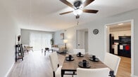 This single-floor residence offers a thoughtfully designed layout with a cohesive, light-filled aesthetic throughout. Light wood-tone flooring flows continuously across the main living areas, creating a sense of visual openness and unity. The combined living and dining area forms the heart of the home, with the dining space accommodating a full-sized table and the living area anchored by a sliding glass door fitted with vertical blinds, allowing ample natural light while providing privacy. A ceiling fan with integrated lighting serves both functional and decorative purposes overhead.

The kitchen is well-appointed with white cabinetry featuring matte black hardware, light countertops, black appliances including a range and dishwasher, and a striking blue subway tile backsplash that adds a bold contrast to the otherwise neutral palette. A window above the sink brings in additional natural light.

The bedroom is a calm retreat with light walls, wood-look flooring, a window with blinds, and a generous double closet with bifold doors offering ample storage. The bathroom features white tile wainscoting, a white vanity with an integrated sink, and wood-look flooring, maintaining the clean, consistent style found throughout the home.