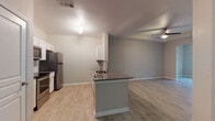 This single-floor residence offers a thoughtfully designed open-concept layout that seamlessly connects the kitchen, dining, and living areas. Light wood-look flooring flows consistently throughout, lending warmth and visual continuity to every room.

The kitchen is a standout feature, equipped with stainless steel appliances including a refrigerator, range, and over-the-range microwave. White shaker-style cabinetry pairs cleanly with dark countertops and a classic white subway tile backsplash. A peninsula island with an integrated sink and bar-height overhang provides both additional prep space and a casual dining option, while an overhead fixture adds focused illumination.

The living area is distinguished by a tray ceiling with a ceiling fan, creating a sense of architectural depth and dimension. Neutral gray walls throughout the space contribute to a calm, cohesive aesthetic that adapts easily to a variety of interior styles.

The bathroom features a wide vanity with dual sinks, a large mirror, gray cabinetry with brushed nickel hardware, and light tile flooring, delivering a clean and functional design. A dedicated laundry area accommodates a full-size washer and offers added everyday convenience.

Overall, the space presents a well-organized, modern interior with consistent finishes and practical amenities suited for comfortable living.