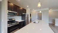 Located at 1000 Solomon Sq in Delaware, Ohio, this single-floor residence offers a thoughtfully designed open-concept layout with contemporary finishes throughout. The kitchen serves as the centerpiece of the home, showcasing a large white quartz island with an undermount sink, rich dark espresso cabinetry, and a full suite of stainless steel appliances including a gas range, over-the-range microwave, and refrigerator. Pendant lighting above the island adds a stylish touch, while recessed lighting illuminates the space efficiently. The kitchen flows seamlessly into the living area, which features durable hardwood-style plank flooring and large windows that invite abundant natural light and outdoor views. The bedroom is generously sized with plush carpeting underfoot and includes a walk-in closet with built-in shelving, offering practical storage solutions. The bathroom is well-appointed with a walk-in shower, dark cabinetry with a quartz-top vanity, and hardwood-style flooring that ties the space together cohesively. A secondary open room with hardwood-style flooring and a window provides flexible use as a living, dining, or office space. Throughout, neutral tones and clean lines create a modern, move-in-ready atmosphere.