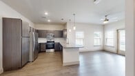 This single-story, 2-bedroom, 2-bathroom residence is thoughtfully designed with a modern aesthetic and functional open-concept layout. The combined kitchen and living area serves as the heart of the home, featuring warm wood-look flooring, recessed lighting, and a ceiling fan. The kitchen is outfitted with dark espresso cabinetry, granite countertops, a white subway tile backsplash, and a full suite of stainless steel appliances including a refrigerator, range, and microwave. A peninsula island with pendant lighting provides additional prep space and casual seating, while windows along the living area invite generous natural light and views of the landscaped exterior grounds.

Both bedrooms are carpeted for comfort and include ceiling fans and windows with blinds. The primary bedroom offers a well-proportioned layout with dedicated closet space. The bathrooms are finished with wood-look tile flooring, dark cabinetry with granite countertops, and a glass-enclosed walk-in shower featuring elegant marble-style tile surround. Each bedroom is served by its own closet for ample storage.

A private patio extends the living space outdoors, overlooking a fenced grassy area with views of the surrounding community. The overall design balances clean, contemporary finishes with a warm and inviting ambiance throughout.