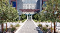 This single-floor amenity space makes a striking first impression with its contemporary exterior, where a geometric patterned façade, a bold red steel canopy, and lush desert landscaping frame a welcoming paver walkway to the entrance. Inside, the grand lobby commands attention with soaring double-height ceilings, floor-to-ceiling windows, and an ornate chandelier suspended above a curated seating arrangement of plush swivel chairs and a richly colored magenta area rug, creating an atmosphere that is both luxurious and inviting. A private dining room offers an intimate yet refined setting, enclosed by expansive glass walls that flood the space with natural light and views of the surrounding streetscape, anchored by a substantial dark wood table beneath a dramatic cluster chandelier with deep teal drapery accents. A dedicated media lounge provides a relaxed retreat, featuring bold textural wallcovering, dual flat-screen displays, and oversized floor seating for a casual, immersive experience. An additional social lounge showcases a mirrored ceiling, floor-to-ceiling glass walls, sculptural pendant lighting, and an eclectic mix of woven and upholstered seating, all set against a dynamic textured wall feature. Together, these spaces reflect a cohesive, design-forward aesthetic tailored for elevated communal living.