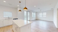 This well-designed 2-bedroom, 2-bathroom home in Austin, TX offers a clean, modern aesthetic throughout its single-floor layout. The open-concept kitchen and living area serves as the heart of the home, featuring crisp white shaker cabinetry, a large central island with white quartz countertops, stainless steel appliances including a refrigerator with ice maker, and a subway tile backsplash. Stylish brass dome pendant lights hang above the island, complementing the recessed lighting overhead. Light wood-tone flooring extends throughout the main living areas, adding warmth to the bright, airy space. The living room benefits from multiple windows and a sliding glass door that invite abundant natural light, along with a ceiling fan for added comfort. The spacious primary bedroom features light wood flooring, dual windows, and a ceiling fan, with a private en-suite bathroom offering a vanity with white cabinetry and access to a dedicated walk-in closet. The secondary bedroom is finished with plush carpet, a ceiling fan, and a sun-filled window. Both bedrooms include generous closet space with built-in shelving and hanging rods. A dedicated laundry room houses a full-size top-load washer and dryer. The overall ambiance is bright, clean, and move-in ready.