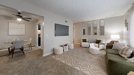 This well-appointed 2-bedroom, 1-bathroom residence is laid out entirely on a single floor, making efficient use of every square foot. The living room features neutral-toned carpet, a wall-mounted television, and a set of decorative arched gold-framed mirrors that add a stylish focal point. Natural light filters in through windows, complementing the warm, inviting palette throughout. Adjacent to the living area, the dining room provides an intimate setting with carpeted flooring and neutral walls. The galley-style kitchen is a standout feature, boasting dark cabinetry contrasted against light countertops and light wood-look flooring, with black appliances lending a bold, contemporary look. The spacious primary bedroom offers generous room for furnishings, soft carpeting, and a closet area large enough to accommodate seating. The second bedroom is equally comfortable. Soft, neutral tones carry throughout both bedrooms, creating a calm and restful atmosphere. The textured ceilings add subtle architectural character consistent across the entire residence. Overall, the space presents a cohesive, cozy design with thoughtful details in every room.
