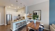 Located at 5840 Farrington Rd in Chapel Hill, NC, this single-floor residence combines contemporary design with functional living spaces. The open-concept layout seamlessly connects the kitchen, dining, and living areas, creating a cohesive and inviting atmosphere throughout.

The kitchen is a standout feature, outfitted with crisp white shaker cabinetry, granite countertops, and a full suite of stainless steel appliances, including a refrigerator, range, and microwave. A peninsula with bar seating and pendant lighting serves as both a prep space and a casual gathering spot. Open floating shelves add additional storage and display space adjacent to the dining area.

The living room is anchored by a bold blue accent wall that adds depth and character to the space. A ceiling fan, access to natural light, and a woven pendant light fixture contribute to the room's relaxed yet polished feel. Wood-look flooring extends throughout the main living areas, providing warmth and continuity.

The bedroom offers a tranquil retreat with large windows that invite natural light and connect to outdoor views. Neutral tones are complemented by a feature wall in a muted blue, adding visual interest. The bathroom includes granite countertops, a tub-shower combination with tile surround, and wood-look flooring, maintaining the home's consistent aesthetic throughout.