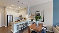 Located at 5840 Farrington Rd in Chapel Hill, NC, this single-floor residence combines contemporary design with functional living spaces. The open-concept layout seamlessly connects the kitchen, dining, and living areas, creating a cohesive and inviting atmosphere throughout.

The kitchen is a standout feature, outfitted with crisp white shaker cabinetry, granite countertops, and a full suite of stainless steel appliances, including a refrigerator, range, and microwave. A peninsula with bar seating and pendant lighting serves as both a prep space and a casual gathering spot. Open floating shelves add additional storage and display space adjacent to the dining area.

The living room is anchored by a bold blue accent wall that adds depth and character to the space. A ceiling fan, access to natural light, and a woven pendant light fixture contribute to the room's relaxed yet polished feel. Wood-look flooring extends throughout the main living areas, providing warmth and continuity.

The bedroom offers a tranquil retreat with large windows that invite natural light and connect to outdoor views. Neutral tones are complemented by a feature wall in a muted blue, adding visual interest. The bathroom includes granite countertops, a tub-shower combination with tile surround, and wood-look flooring, maintaining the home's consistent aesthetic throughout.