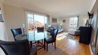 This single-floor, 1-bedroom, 1-bathroom residence in Delaware offers a well-organized and comfortable layout filled with natural light throughout. The combined living and dining area serves as the heart of the home, featuring warm hardwood flooring, crown molding, and large windows that invite generous sunlight. A sliding glass door connects the living space to the outdoors, framing pleasant exterior views. The dining area accommodates a round glass-top table with upholstered chairs, while the living room provides a cozy setting with a cushioned sofa, decorative wall art, and a wall-mounted television. The kitchen is outfitted with warm wood cabinetry, a gas range, full-size refrigerator, and a single-basin sink beneath a window overlooking the outdoors. The bedroom is spacious and bright, benefiting from multiple windows, hardwood floors, a ceiling fan, and ample room for furnishings. A second, more intimate sleeping area offers a quiet retreat with a large window and warm natural light. The full bathroom features retro-style peach tile surrounding the tub-shower combination, a mosaic tile floor, white vanity with storage, and a bright window. Throughout the residence, the consistent use of hardwood floors and neutral tones creates a cohesive and inviting atmosphere.