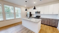 Located at 8214 Springdale Rd in Louisville, KY, this two-story home offers three bedrooms and four bathrooms across two well-appointed floors. The main level centers around an open-concept kitchen and living area, where light hardwood-style flooring flows throughout. The kitchen is a standout, featuring a large central island with a granite countertop, undermount sink, and pendant lighting. White upper cabinetry contrasts with wood-toned lower cabinets, complemented by stainless steel appliances and a clean white backsplash. Natural light pours in through multiple windows, enhancing the bright, airy ambiance. A pantry and a half-bath round out the main floor. The upper level, which comprises the larger portion of the home, houses all three bedrooms, including a generously sized primary suite with a walk-in closet featuring built-in shelving and a natural light source. Additional bedrooms offer neighborhood views through large double windows and warm hardwood-style flooring. The bathrooms are finished with granite-topped vanities and matching wood-tone cabinetry. A hallway and additional closet space provide practical storage. The home's clean, contemporary design and consistent finishes create a cohesive and functional living environment throughout.