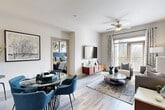 This single-floor residence offers a thoughtfully designed open-concept layout that seamlessly connects the living, dining, and kitchen areas. The living room is anchored by a bold blue accent wall, light wood-style flooring, large windows that invite natural light, and a ceiling fan overhead. A dedicated dining area with a glass-top table flows naturally into the space, while the living area provides a comfortable and stylish setting with garden views.

The kitchen is a standout feature, showcasing rich dark espresso cabinetry with glass-front upper panels, granite countertops, a kitchen island with pendant lighting, and a full suite of stainless steel appliances including a refrigerator, electric range, microwave, and dishwasher. Track lighting and a raised ceiling detail add architectural interest.

The generously sized bedroom features large windows with outdoor views, light wood-style flooring, a tray ceiling accent, and access to both a walk-in closet and an en-suite bathroom. The primary bathroom offers dark cabinetry, granite countertops, a dual-sink vanity, tile flooring, and a soaking tub. A secondary full bathroom provides a tub-shower combination with tile surround, a granite-topped vanity, and matching dark cabinetry, maintaining a consistent design language throughout.