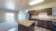 Located on 25th St S in Fargo, North Dakota, this one-bedroom, one-bathroom unit offers a thoughtfully designed single-floor layout that maximizes comfort and functionality. The kitchen is a standout feature, boasting rich dark wood cabinetry, granite-style countertops, stainless steel appliances including a range, microwave, dishwasher, and refrigerator, and wood-look flooring that adds warmth and durability. A peninsula provides additional counter space and serves as a natural transition into the open living area. The living room features plush carpeting, baseboard heating, and a sliding glass door that opens onto a private balcony with outdoor views — filling the space with natural light. The bedroom is a comfortable retreat with soft carpet, baseboard heating, and a window that brings in additional daylight. The bathroom is finished with wood-look flooring, dark cabinetry, granite-style countertops, a single vanity with a large mirror, and a full tub-shower combination. A dedicated laundry room houses a full-size washer and dryer with overhead wire shelving for added storage. Neutral tones and clean finishes throughout create a cohesive, move-in-ready atmosphere.