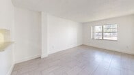 Located at 15401 NE 6th Ave in Miami, FL, this thoughtfully designed one-bedroom, one-bathroom residence offers a bright and modern living experience on a single floor. Light-tone large-format tile flooring runs consistently throughout the home, complementing the crisp white walls and textured ceilings that lend a clean, contemporary feel to every room.

The combined dining and living area is an open, airy space filled with natural light from a large window, providing a versatile setting for both relaxing and entertaining. A gold-accented pass-through window adds a subtle decorative touch between the living area and kitchen.

The galley-style kitchen is well-appointed with sleek white cabinetry, light quartz countertops, a stainless steel sink, and stainless steel appliances including a refrigerator and range, making efficient use of the available space.

The bedroom is a comfortable, well-lit room with a dedicated window that invites natural light, along with convenient access to closet storage. Multiple closets throughout the unit provide ample storage options.

The bathroom features an elegant marble-patterned surround encasing a full soaking tub and shower combination, paired with a quartz vanity surface, creating a polished and spa-like atmosphere. A hallway connects the rooms, keeping the layout practical and easy to navigate.