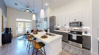 Located in Dallas, TX, this thoughtfully designed 2-bedroom, 3-bathroom residence offers a cohesive blend of modern style and functional living across a single floor. The open-concept kitchen serves as the heart of the home, boasting a large island with a built-in sink, pendant lighting, white upper cabinetry, contrasting gray lower cabinets, a marble-style tile backsplash, and stainless steel appliances. The kitchen flows naturally into the living area, which benefits from high ceilings, a ceiling fan, and access to natural light through large windows and glass doors. Each bedroom is distinctly styled and features large windows that invite outdoor views and natural light, with durable wood-style flooring throughout. One bedroom features a muted sage green accent wall, while the other showcases a deep moody tone, adding character to each space. Both bedrooms include dedicated closets for organized storage. The bathrooms are finished with clean, modern details, including one featuring a dual-sink vanity with dark hardware, white tile tub surround with matte black fixtures, and direct access to a walk-in closet. The overall ambiance is contemporary and inviting, with consistent use of neutral tones and quality finishes throughout.