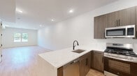 Located at 100 Shepherds Ln in Totowa, NJ, this thoughtfully designed 2-bedroom, 2-bathroom residence offers a clean, modern aesthetic throughout its generously sized single-floor layout. Light-toned hardwood flooring flows seamlessly across the living spaces, complemented by crisp white walls and recessed lighting that create a bright, welcoming ambiance.

The open-concept kitchen and living area serves as the heart of the home, featuring a large waterfall-edge island with an undermount sink, warm wood-toned cabinetry, quartz countertops, and a full suite of stainless steel appliances including a gas range, microwave, and refrigerator. The space is well-lit with recessed lighting and connects naturally to the living area.

Both bedrooms are generously proportioned, bathed in natural light through double-pane windows that frame views of surrounding greenery. The primary bedroom includes access to a dedicated walk-in closet outfitted with built-in shelving and hanging rods for ample storage.

The two bathrooms are finished in a contemporary style, featuring large-format floor tiles, white subway-tiled walls, and matte black hardware accents. One bathroom offers a soaking tub with a sliding glass enclosure, while the other includes a walk-in glass shower. Built-in shelving adds functional storage to both spaces.