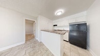 Located at 705 S Beach St in Daytona Beach, Florida, this efficiently designed one-bedroom, one-bathroom unit offers a practical and well-organized single-floor layout. The open-concept living and kitchen area is bright and airy, finished with large-format neutral tile flooring throughout and crisp white walls that reflect natural light streaming in through double-hung windows. A wall-mounted mini-split system provides dedicated climate control to the main living space.

The kitchen is defined by a peninsula with a stone-look countertop that serves both as a workspace and casual dining surface. White shaker-style cabinetry offers ample storage, while the space accommodates a full-size black refrigerator, an under-cabinet range hood, and a single-basin sink. A textured popcorn ceiling adds a classic touch throughout the unit.

The bedroom is a comfortable, well-proportioned room featuring a ceiling fan with light fixture, a window with natural light, and continued tile flooring. It connects directly to the bathroom, which includes a white vanity with an integrated sink, mirror, and tile flooring. A dedicated utility room provides additional functional space, housing the water heater and utility connections. This unit offers a clean, move-in-ready environment in a central Daytona Beach location.