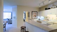 Located at 400 Stone Lion Dr in Durham, this single-story residence offers a thoughtfully designed interior centered around an open-concept layout. The kitchen is a standout feature, equipped with white cabinetry, a smooth countertop, and a curved breakfast bar with barstool seating — ideal for casual dining or entertaining. Track lighting overhead provides focused illumination throughout the kitchen area, complementing the natural light that filters in from adjacent rooms. A tile backsplash adds a clean, finished look to the cooking space. The open passthrough design connects the kitchen seamlessly to the surrounding living areas, creating a sense of flow and accessibility throughout the home. Neutral wall tones and light carpeting contribute to a warm, cohesive aesthetic across the space. A glimpse into the adjoining bedroom reveals a bright, comfortable room with a window, while the hallway features a classic barn-style door that adds a subtle decorative touch. Wall-mounted artwork and understated décor enhance the overall ambiance, making this residence feel both functional and inviting.