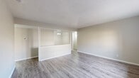 Located at 6 Beldoir Ct in Hot Springs, Arkansas, this single-story unit offers a clean, updated interior with a neutral color palette throughout. The living areas feature light gray wood-look vinyl flooring and are separated by a distinctive half-wall pass-through with glass panels above, creating an open, connected feel while maintaining visual definition between spaces. A textured ceiling adds subtle character to the main living area, which also benefits from a window that draws in natural light.

The galley-style kitchen is efficiently laid out, featuring white cabinetry, light countertops, wood-look flooring, and black appliances including a refrigerator, range, and dishwasher. Additional storage is accessible via a door at the end of the kitchen corridor.

The bedrooms are carpeted for comfort and each includes a ceiling fan with light fixture and a window offering views of the surrounding exterior. The neutral walls and soft carpet tones maintain a calm, cohesive atmosphere.

The bathrooms are consistently appointed with wood-look vinyl flooring, white vanity cabinetry with light stone-style countertops, large mirrors, white tile tub/shower surrounds, and closet access nearby. The overall interior presents a well-maintained, move-in-ready environment throughout.