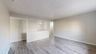 Located at 6 Beldoir Ct in Hot Springs, Arkansas, this single-story unit offers a clean, updated interior with a neutral color palette throughout. The living areas feature light gray wood-look vinyl flooring and are separated by a distinctive half-wall pass-through with glass panels above, creating an open, connected feel while maintaining visual definition between spaces. A textured ceiling adds subtle character to the main living area, which also benefits from a window that draws in natural light.

The galley-style kitchen is efficiently laid out, featuring white cabinetry, light countertops, wood-look flooring, and black appliances including a refrigerator, range, and dishwasher. Additional storage is accessible via a door at the end of the kitchen corridor.

The bedrooms are carpeted for comfort and each includes a ceiling fan with light fixture and a window offering views of the surrounding exterior. The neutral walls and soft carpet tones maintain a calm, cohesive atmosphere.

The bathrooms are consistently appointed with wood-look vinyl flooring, white vanity cabinetry with light stone-style countertops, large mirrors, white tile tub/shower surrounds, and closet access nearby. The overall interior presents a well-maintained, move-in-ready environment throughout.