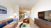 This thoughtfully designed one-bedroom, one-bathroom unit offers an efficient and functional layout across a single floor. The open-concept living and kitchen area serves as the heart of the unit, where light wood-tone cabinetry, a subway tile backsplash, and stainless steel appliances — including a French door refrigerator, range, microwave, and dishwasher — define a modern kitchen. A white quartz island with built-in cabinetry and bar seating provides additional prep space and casual dining. Light wood-look flooring flows throughout the main living area, enhancing the bright, airy atmosphere created by recessed lighting and a glass-paneled exterior door that fills the living room with natural light.

The bedroom is a comfortable retreat, featuring plush carpet, a ceiling fan, and windows that allow natural light to filter in. It connects directly to the full bathroom, which includes a glass-enclosed walk-in shower with large-format tile, matte black fixtures, and a wooden bench. Adjacent to the bathroom is a dedicated walk-in closet with built-in rod and shelf storage. Clean white walls and a neutral palette throughout create a cohesive, modern ambiance well-suited for everyday living.