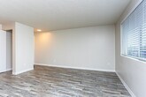 Located at 3418 90th St S in Lakewood, Washington, this single-floor residence offers a clean, functional layout designed for comfortable living. The interior features smooth, neutral-toned walls and durable hardwood-style plank flooring throughout, providing a cohesive and low-maintenance aesthetic.

The living area is open and airy, benefiting from multiple windows that invite natural light and offer views of the surrounding neighborhood. A baseboard heating system runs along the exterior wall, ensuring warmth during cooler Pacific Northwest months. The textured ceiling adds a classic touch to the space.

The kitchen is efficiently designed with white cabinetry, countertops, and white appliances including a range and refrigerator. An overhead light fixture provides ample task lighting. The kitchen opens visually toward the main living area, creating a connected and accessible flow between the two spaces.

Overall, the unit presents a straightforward, move-in-ready environment with consistent finishes throughout. The neutral color palette and practical layout make it a versatile space well-suited for a variety of living arrangements.