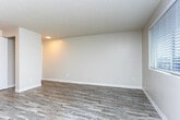 Located at 3418 90th St S in Lakewood, Washington, this single-floor residence offers a clean, functional layout designed for comfortable living. The interior features smooth, neutral-toned walls and durable hardwood-style plank flooring throughout, providing a cohesive and low-maintenance aesthetic.

The living area is open and airy, benefiting from multiple windows that invite natural light and offer views of the surrounding neighborhood. A baseboard heating system runs along the exterior wall, ensuring warmth during cooler Pacific Northwest months. The textured ceiling adds a classic touch to the space.

The kitchen is efficiently designed with white cabinetry, countertops, and white appliances including a range and refrigerator. An overhead light fixture provides ample task lighting. The kitchen opens visually toward the main living area, creating a connected and accessible flow between the two spaces.

Overall, the unit presents a straightforward, move-in-ready environment with consistent finishes throughout. The neutral color palette and practical layout make it a versatile space well-suited for a variety of living arrangements.