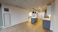 Located at 675 N Wells St in Chicago's vibrant River North neighborhood, this single-floor unit combines industrial design elements with contemporary finishes throughout. The exposed concrete ceilings serve as a defining architectural feature, lending an urban loft aesthetic that contrasts beautifully with the clean, modern interiors below.

The open-concept living and kitchen area is anchored by a well-appointed kitchen featuring two-tone cabinetry — grey lower cabinets paired with white uppers — complemented by white quartz countertops, a herringbone tile backsplash, and a full suite of stainless steel appliances. A central island with pendant lighting provides additional prep space and a natural gathering point. Light wood-tone flooring runs throughout, adding warmth to the space.

The bedroom area benefits from expansive floor-to-ceiling windows framed in black, offering striking elevated views of the Chicago skyline and surrounding River North architecture. Recessed lighting and natural light combine to keep the space bright throughout the day. A spacious walk-in closet with built-in shelving provides ample storage.

The bathroom features white subway tile surrounding a soaking tub, matte black fixtures and hardware, large-format floor tile, and grey cabinetry with gold hardware — continuing the sophisticated, modern aesthetic found throughout the unit.