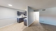Located at 1905 W 40th St in Davenport, Iowa, this two-bedroom, one-bathroom unit offers a practical and well-organized single-floor layout. The living area features plush carpeting and a window with natural light, complemented by a window AC unit. It flows openly into the kitchen, which is separated by a half-wall peninsula. The kitchen is equipped with dark gray cabinetry, white countertops, a double-basin sink with a matte black faucet, a white electric range, and a refrigerator, all set on tile flooring. Both bedrooms are carpeted and finished in light gray tones. The primary bedroom is generously sized and includes two closets — one standard and one larger — providing ample storage. The second bedroom also benefits from natural light via a window with blinds. A hallway connects the bedrooms to the shared bathroom, which features wood-look vinyl flooring, a dark wood vanity with a white countertop, a toilet, and a tub-shower combo with a curved curtain rod. The unit maintains a clean, neutral palette throughout, with light blue-gray walls and white trim creating a consistent and functional aesthetic.