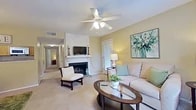 This single-floor, 2-bedroom, 2-bathroom residence at 7820 Millicent Way in Shreveport, Louisiana offers a comfortable and functional layout. The living room serves as the heart of the home, featuring a wood-paneled fireplace with a white mantle, ceiling fan with light fixture, and plush carpeting. Natural light filters in through windows dressed with teal curtains, and a glass-top coffee table anchors the seating area. An exterior door provides convenient outdoor access directly from the living space. The adjoining dining area includes a stylish chandelier and louvered bifold closet doors, adding practical storage. The kitchen is equipped with wood cabinetry, stone-look countertops, and standard appliances including a range, overhead microwave, and ample counter space. The primary bedroom offers a ceiling fan, natural light from a window with drapes, and a dedicated closet. The second bedroom is equally comfortable, also featuring a ceiling fan and window with natural light. Both bedrooms are carpeted. Two closets provide organized storage, including one spacious walk-in style with built-in shelving. The two bathrooms are functional and tidy, with one featuring wood-tone vanity cabinetry, stone-look countertops, and a shower/tub combination. A connecting hallway links the bedrooms and bathrooms seamlessly.