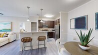 This well-appointed two-bedroom, three-bathroom single-floor residence at 2015 Gum Branch Rd in Jacksonville, NC offers a thoughtfully designed layout with modern finishes throughout. The open-concept kitchen is a standout feature, showcasing rich dark cabinetry, granite countertops, stainless steel appliances including a refrigerator, range, microwave, and dishwasher, along with a breakfast bar with pendant lighting that flows seamlessly into the dining area. The dining space is an intimate setting with chair-rail molding and crown molding details. The living room is bright and welcoming, featuring crown molding, a ceiling fan, and natural light from large windows. Light-toned hardwood-style flooring runs throughout the home, complementing the neutral color palette. Both bedrooms are generously sized, each with ceiling fans; the primary bedroom includes a spacious walk-in closet with built-in shelving. The second bedroom benefits from multiple windows that fill the room with natural light. All three bathrooms are finished with wood-tone vanities and granite countertops. A dedicated laundry/utility room provides additional functionality. Crown molding and consistent finishes lend a cohesive, polished character to this well-designed residence.